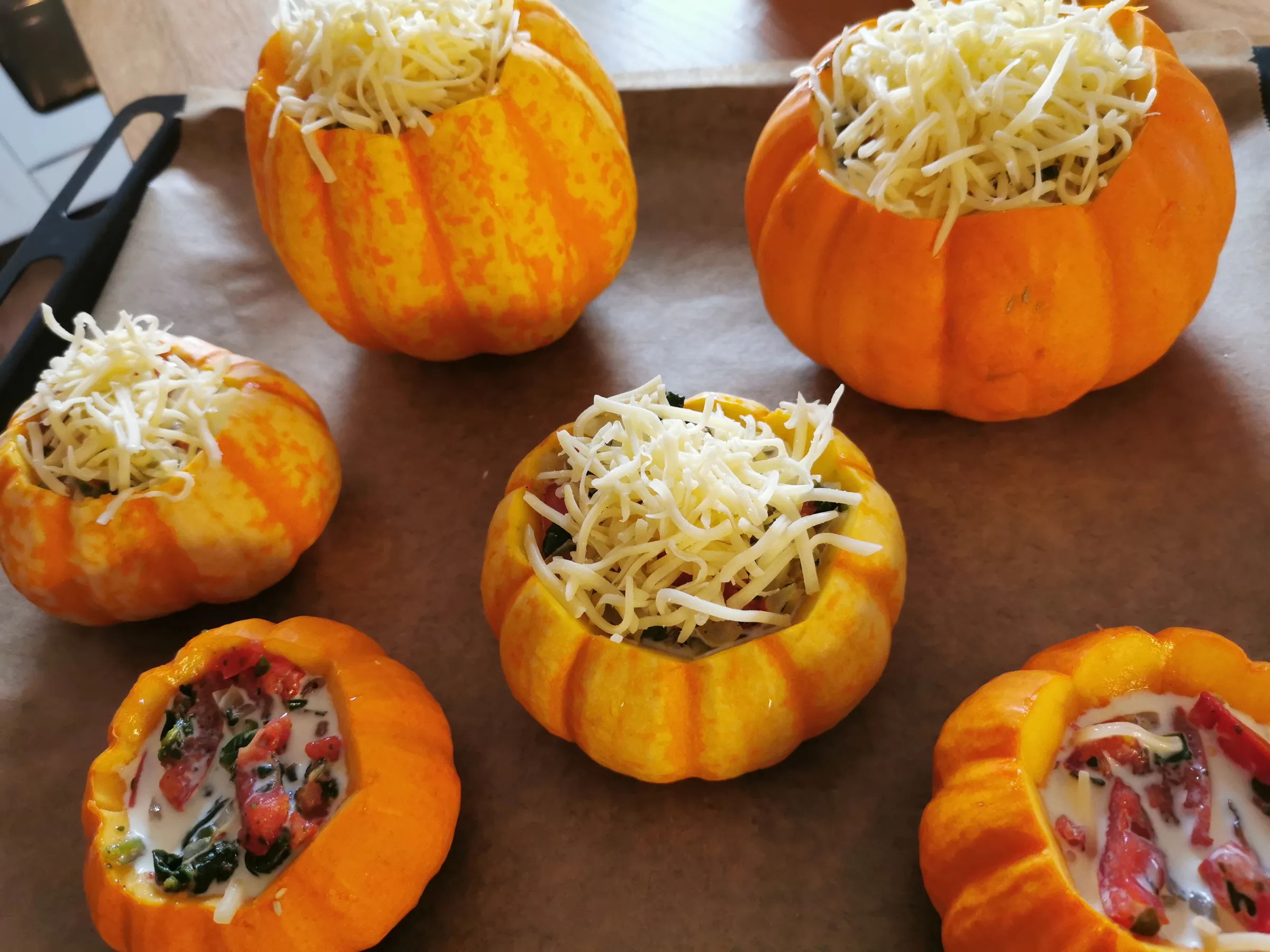 Kleine bunte Kürbisse, gefüllt mit Gemüse und mit Käse bestreut, auf dem Backblech